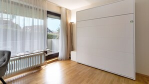 Une pièce dotée d’un placard à portes coulissantes, d’un radiateur, d’une chaise et offrant une vue sur l’extérieur à travers une fenêtre orn ée de rideaux légers.
