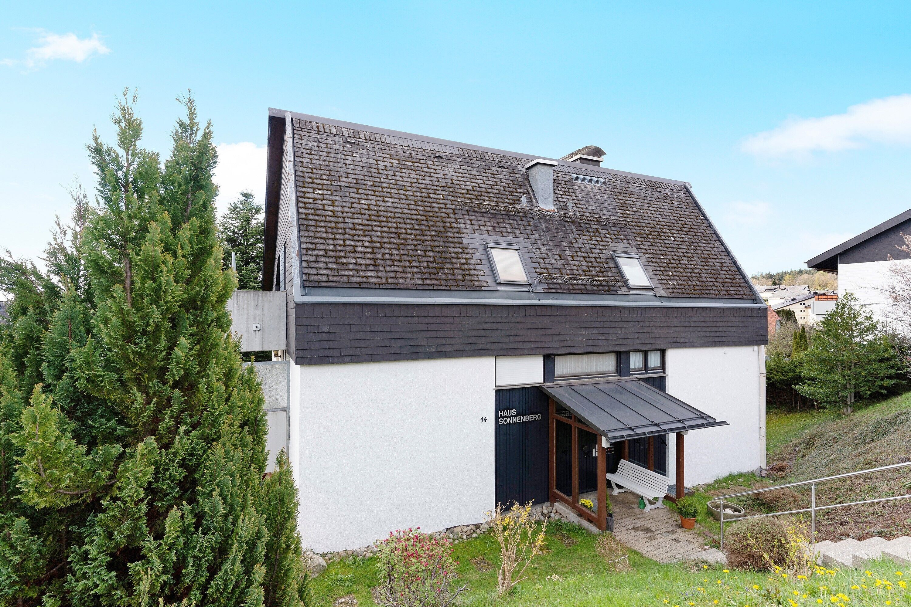 Ein modernes Haus mit einem geneigten Dach, einer kleinen Veranda und einer sichtbaren Tür.