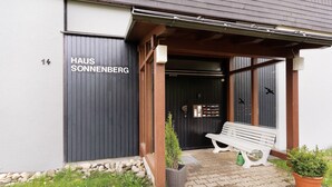 Un bâtiment sur lequel on peut lire l’inscription « HAUS SONNENBERG », un banc en bois et des plantes en pot.