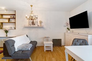 Una sala de estar moderna con un sofá gris, una mesa blanca, un televisor montado en la pared y una araña.