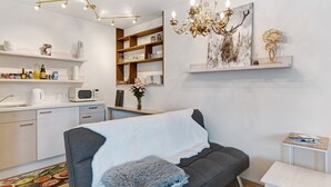 Un salon moderne avec un canapé gris, une table basse blanche, un lustre, un four à micro-ondes et une bibliothèque.