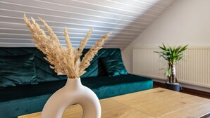 A modern living room with a wooden coffee table, a unique white vase with dried plants, a green sofa, and a potted plant.