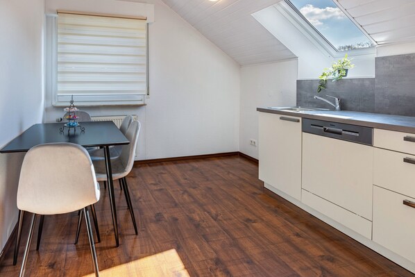 Une cuisine compacte dotée d’un puits de lumière, un coin repas avec une table et des chaises, et un lave-vaisselle encastré.