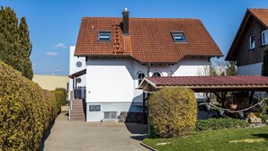 A two-story house with a tiled roof, a covered porch, and a paved driveway.