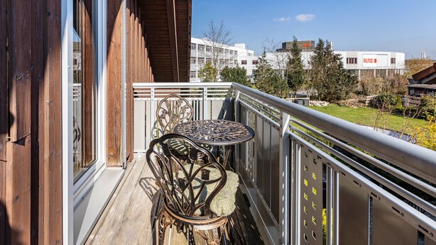 A balcony with a metal table and chairs, wooden railings, and a view of buildings and trees.