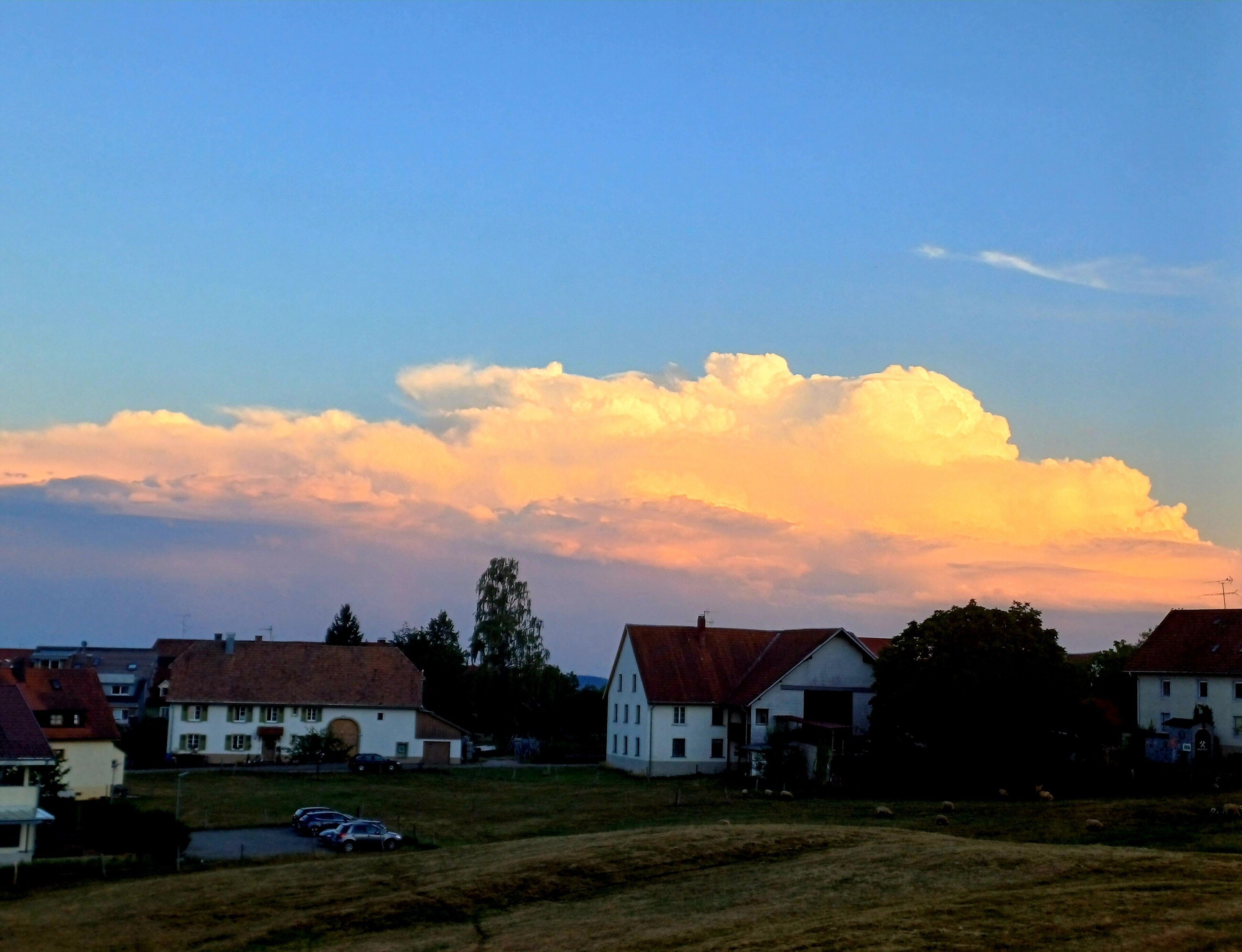 Un paysage rural avec des maisons, un champ et un grand nuage dans le ciel.