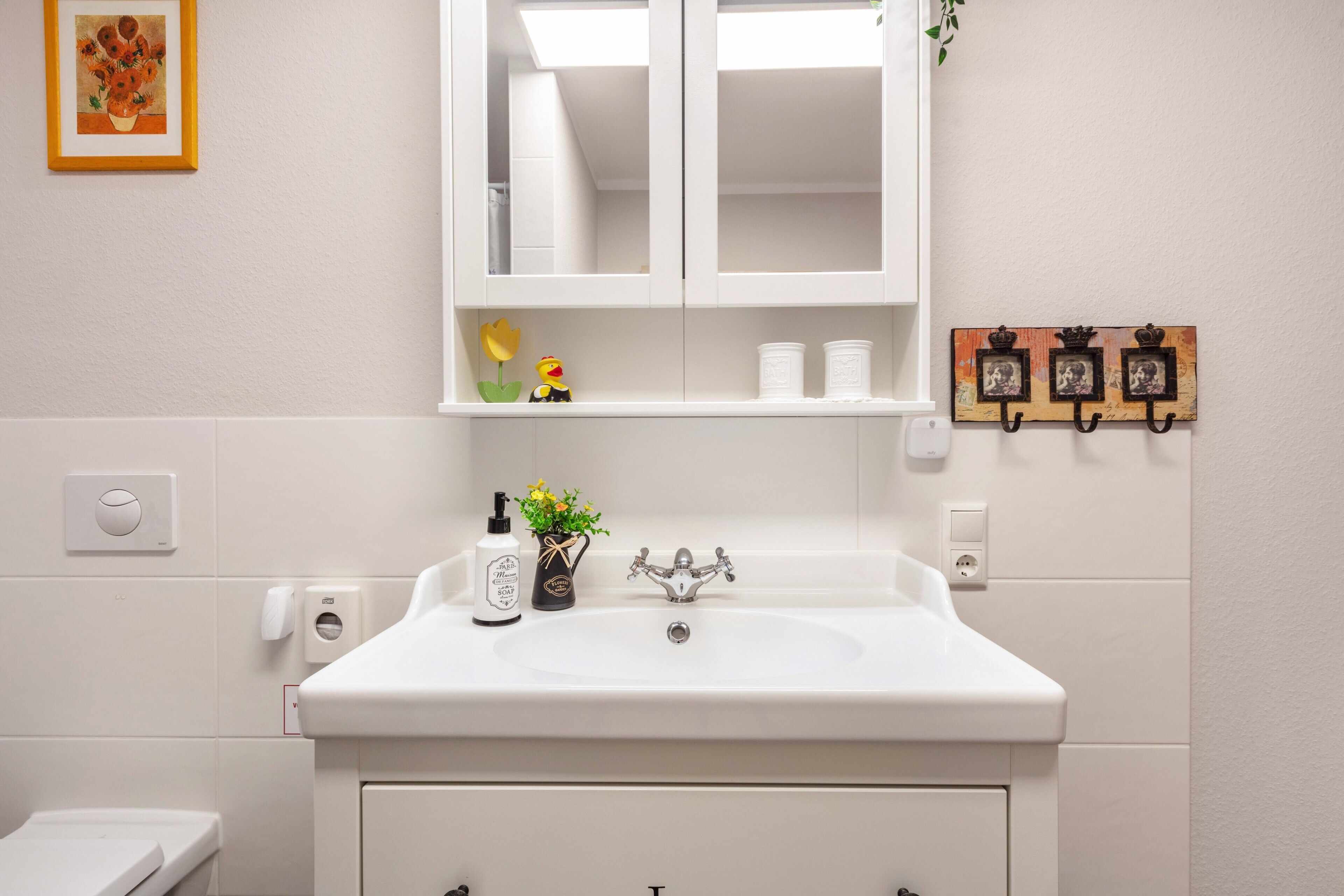 A bathroom with a white sink, a mirror, a toilet, and a shelf with toiletries.