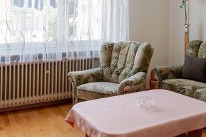 Una habitación con un radiador, un sillón estampado con motivos florales, un sofá a juego y una mesa con mantel rosa.