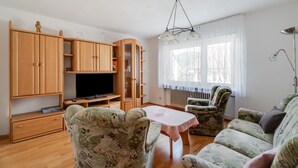 A living room with a wooden cabinet, a television, a table, and two patterned armchairs.