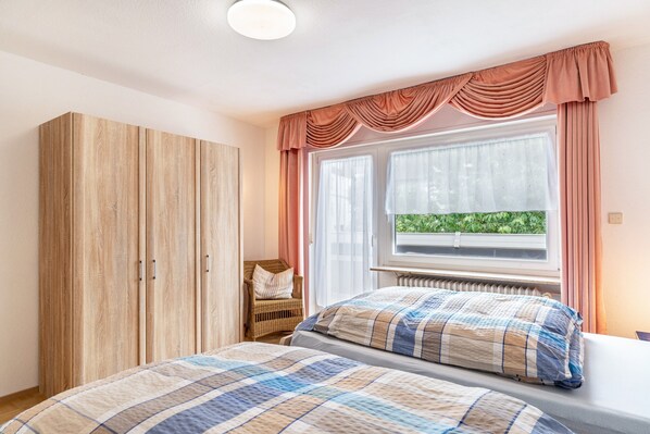 A bedroom with a bed, a wardrobe, a window with curtains, and a view of greenery outside.
