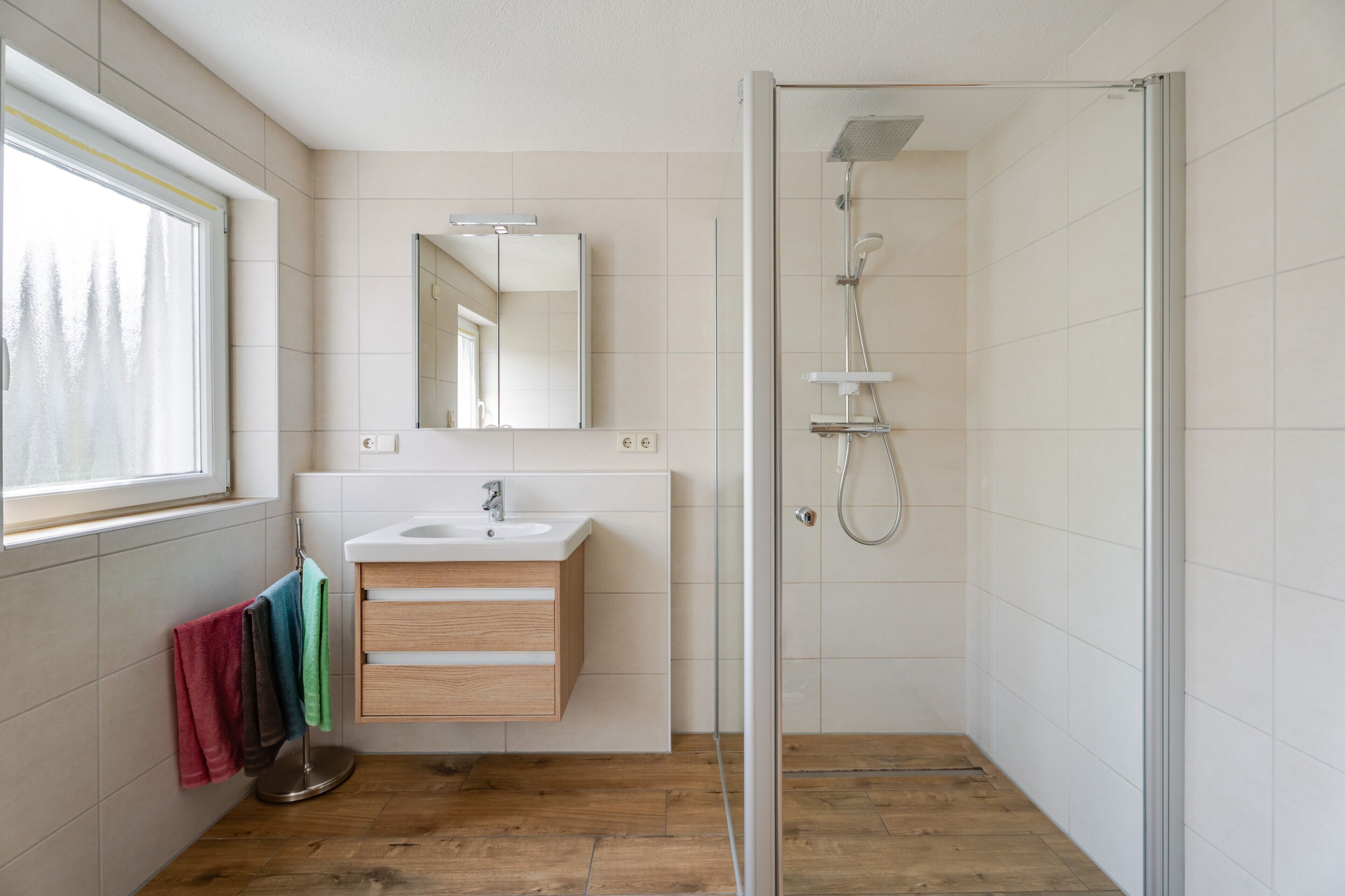 Ein modernes Badezimmer mit Duschkabine aus Glas, einem Holzkosmetikschrank mit Waschbecken und einem Spiegel darüber.