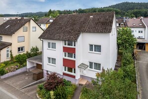 Ein mehrgeschossiges Wohnhaus mit Schrägdach, roter Tür und kleinem Vorgarten.