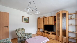 Ein Wohnzimmer mit Holzschrank, Fernseher und einem blumengemusterten Sessel.