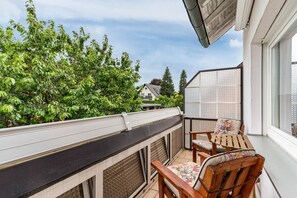 A balcony with a table and chairs, a view of trees, and a house in the background.