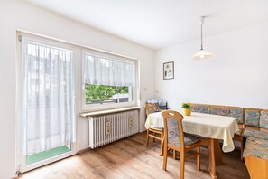 A dining area with a table, chairs, a bench, a radiator, and a window with curtains.