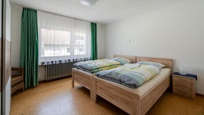 A bedroom with a wooden bed, a nightstand, a radiator, and a window with curtains.