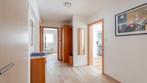 A hallway with wooden flooring, a wooden cabinet, a mirror, and a door leading to a bathroom.