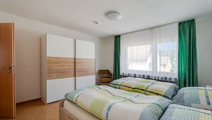 Ein Schlafzimmer mit einem Bett, einem Kleiderschrank, einem Fenster mit Vorhängen und einer Deckenleuchte.