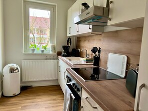Une cuisine moderne avec une fenêtre, des meubles blancs, une cuisinière et un radiateur.