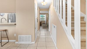 A hallway with a kitchen area on the left, a dining area in the center, and a staircase on the right. - Sunray - Gulf-side townhouse, beach access & pool (Navarre)