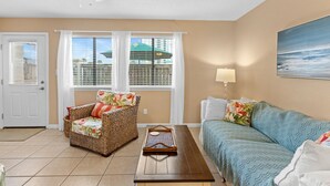 A living room with a wicker chair, a wooden coffee table, a sofa, and a painting on the wall. - Sunray - Gulf-side townhouse, beach access & pool (Navarre)