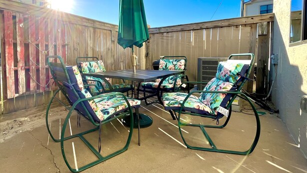 Une terrasse extérieure avec une table et des chaises, un parasol vert et une clôture en bois.