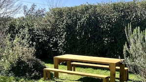 Een houten picknicktafel met banken in een gazon, omringd door dichte struiken.
