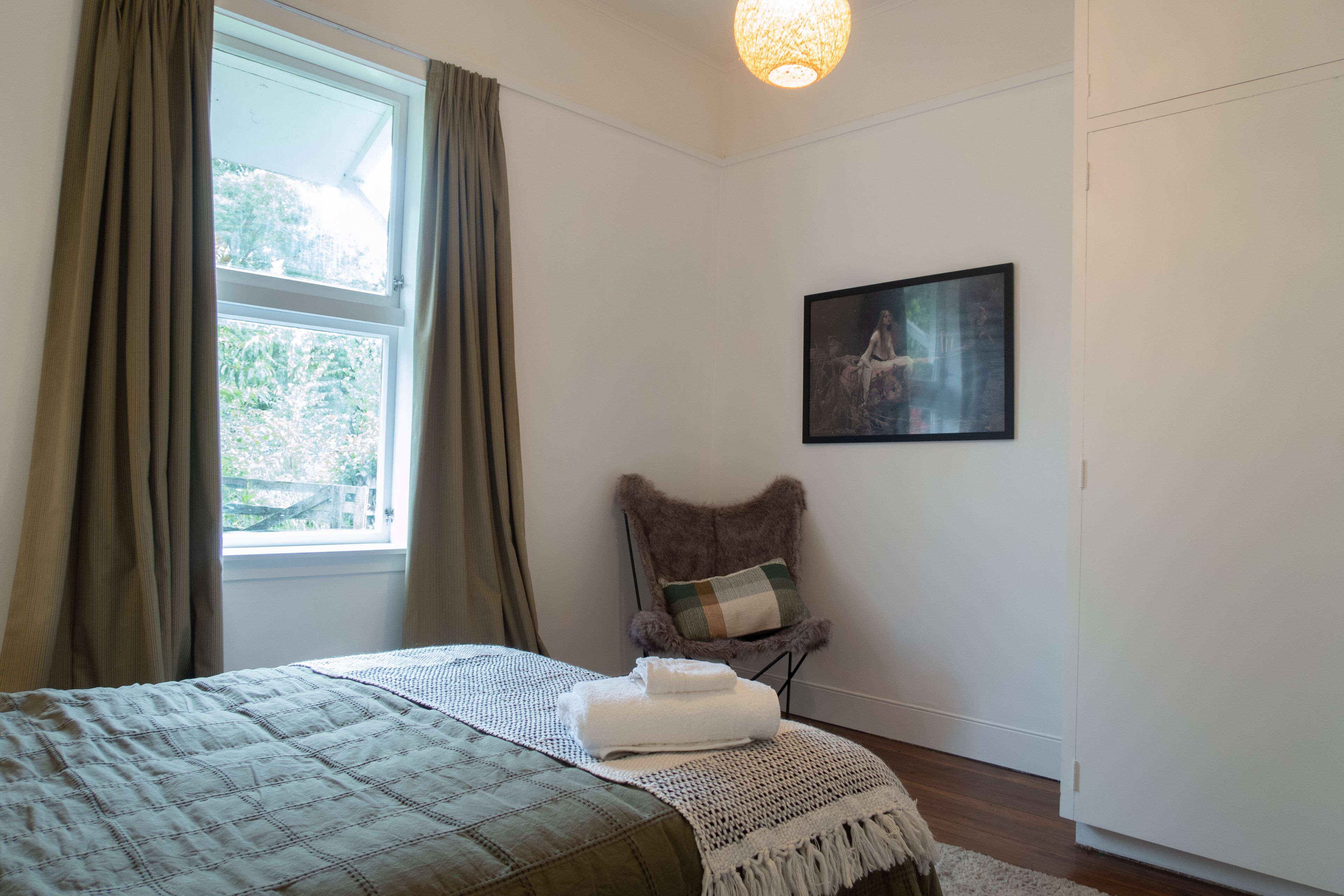 Een slaapkamer met een bed, een stoel, een schilderij en een raam met gordijnen.