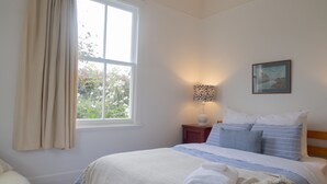 Een slaapkamer met een groot raam, een nachtkastje met een lamp en een bed met gestreept beddengoed.