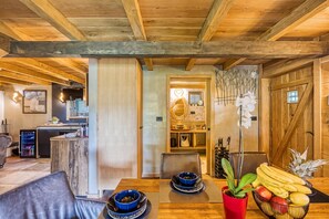 Un intérieur chaleureux avec une table à manger en bois, des chaises et un coin cuisine visible à travers une porte ouverte.