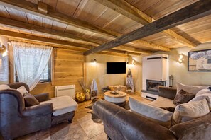 Un salon chaleureux avec des poutres en bois, des canapés en cuir, une cheminée et un téléviseur à écran plat.