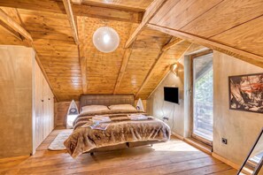 Une chambre confortable avec un plafond en bois, un lit recouvert d’une couverture à rayures, une table de chevet et une fenêtre donnant sur un beau paysage.