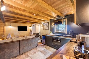 A modern kitchen with a built-in oven, a dining area with a sofa, and a TV mounted on the wall.