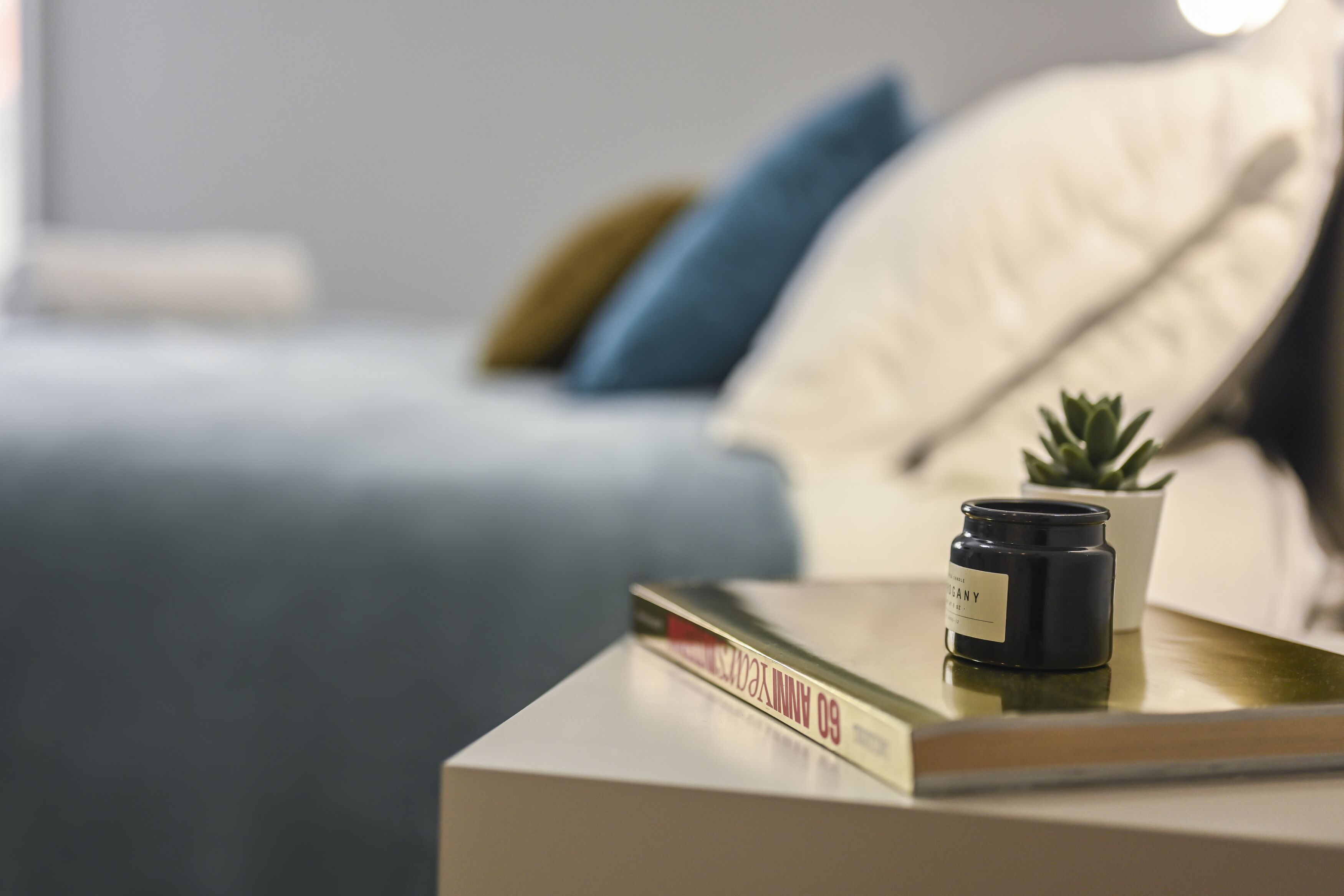 A bedside table with a book, a candle, and a small potted plant.