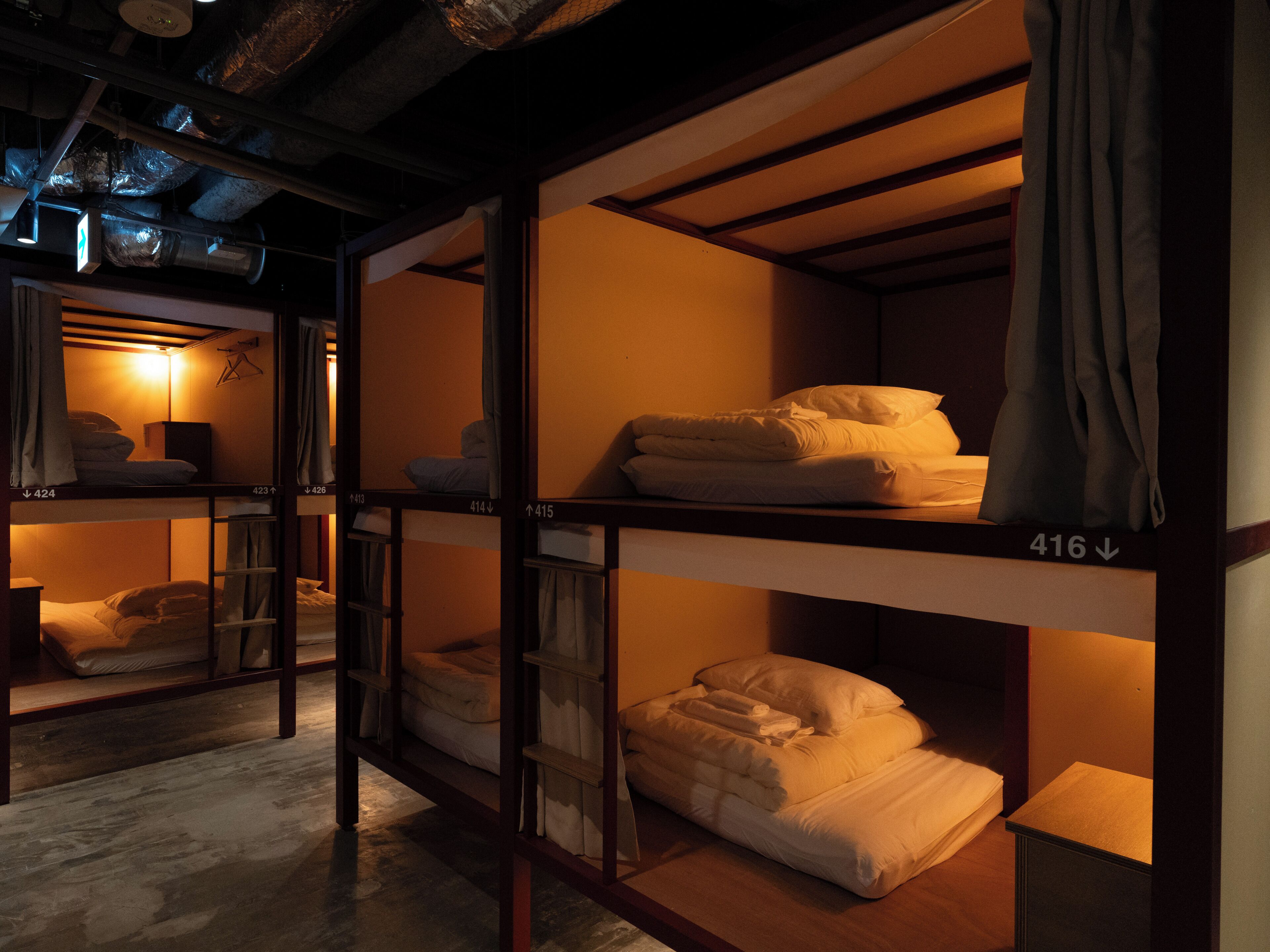 A row of bunk beds with numbers on the side, a hanging light fixture, and a wooden floor.