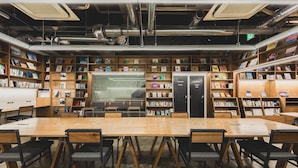 Una biblioteca con scaffali in legno, un tavolo grande e sedie nere.