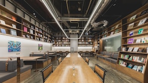 Una moderna biblioteca con tavoli di legno ed scaffali, che presenta un lungo tavolo centrale e zone relax.