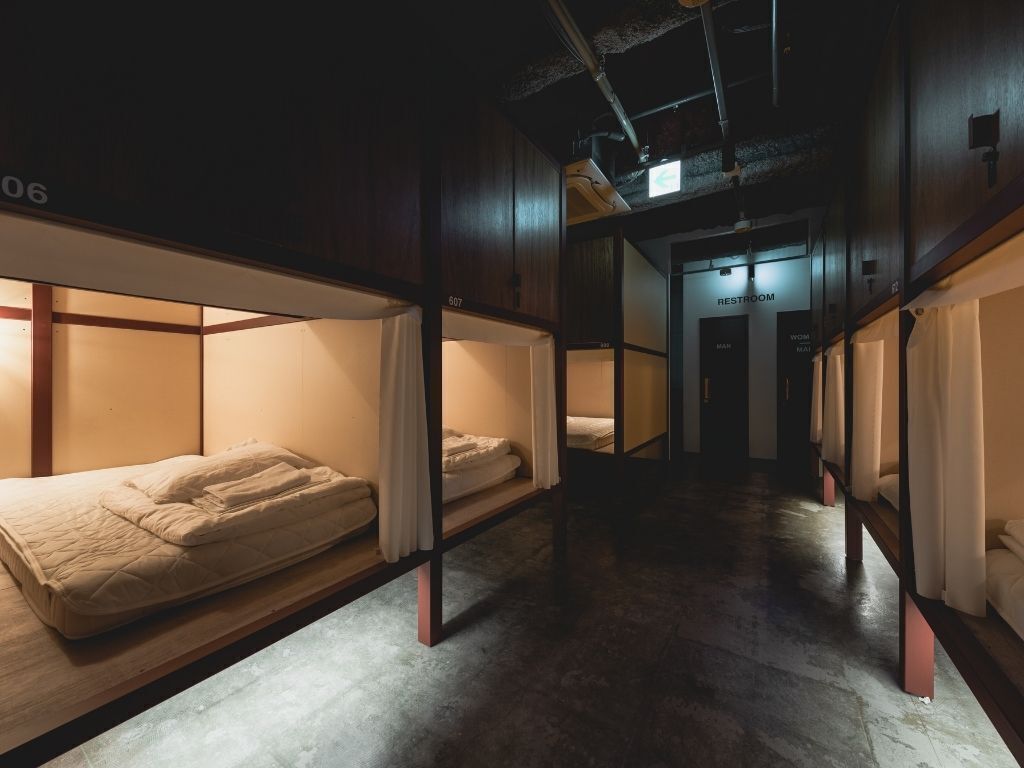 A corridor with bunk beds, a visible restroom sign, and a concrete floor.