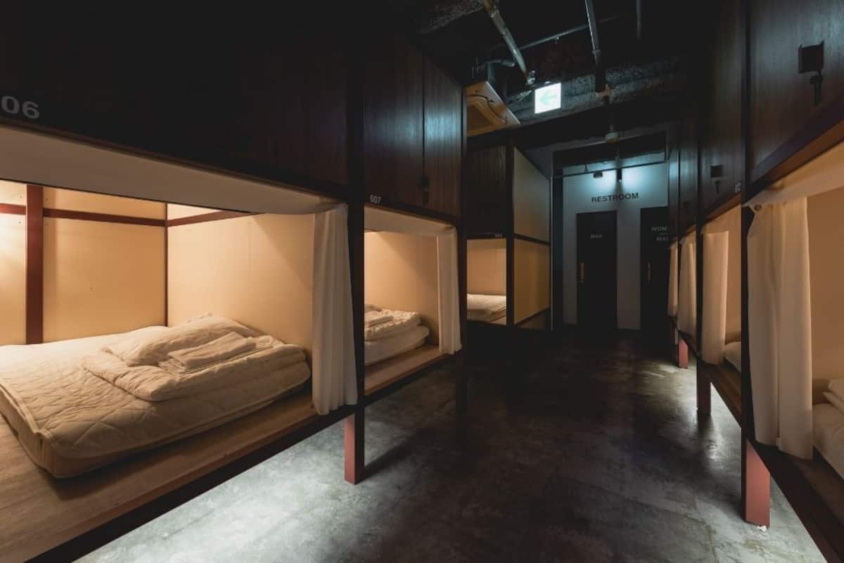 Un pasillo con literas, un letrero visible de baño y suelo de concreto.