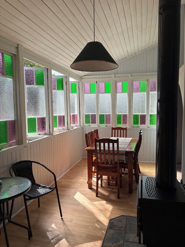 A dining area with a table and chairs, a hanging light fixture, and a view through a window with patterned glass. - Tablelands Tranquil Retreat (Jaggan)