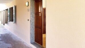 A hallway with a wooden door, a wall-mounted light, and a number plate.