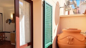 A room with a window, a green shutter, and a large terracotta pot.