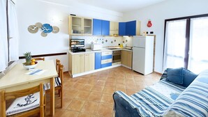 A compact kitchen with blue and white cabinets, a microwave, a refrigerator, and a dining table with chairs.