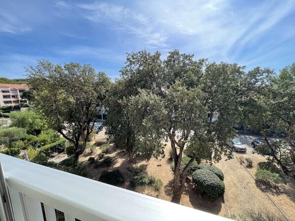 A balcony with a view of a courtyard featuring trees and a parking area.