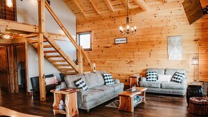 A wooden interior with two sofas, a staircase, and a chandelier. - Stunning Hocking Hills Views, Huge Skies ~ Sauna, Pet Friendly, Hot Tub, WiFi (new plymouth)