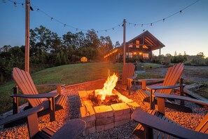 A fire pit with chairs and a wooden structure in the background.