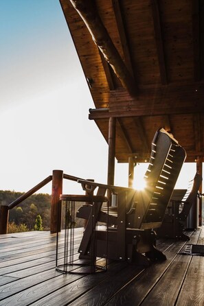 A wooden deck with a metal chair and a table, overlooking a forested landscape.