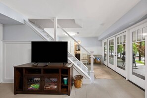 A living room with a flat-screen TV on a wooden cabinet, a staircase, and a sliding glass door leading to an outdoor area. - Perfect Weekend Getaway- Lake Arrowhead Home-Lakefront-Private Dock-Pet Friendly-Pool & Tennis (Waleska)