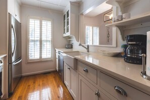 Una cocina con refrigerador de acero inoxidable, cafetera y ventana con persianas.