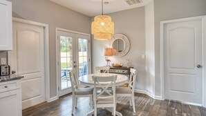 A kitchen with white cabinets, a dining table with chairs, a hanging light fixture, and a round mirror on the wall. - Fire pit, Pet Friendly, Only 1 Mile to Beach, 4 Miles to Historic Downtown, $300 in Free Tickets! (St. Augustine)
